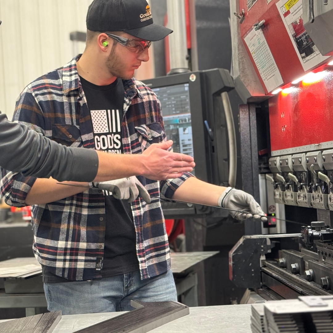 Image of a K-State Salina student while working at Great Plains, feeding a piece of metal into a machine. 