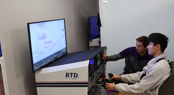 A flight instructor at K-State Salina motions to one of the campus's many flight simulators, while a summer camper flies a simulator plane.