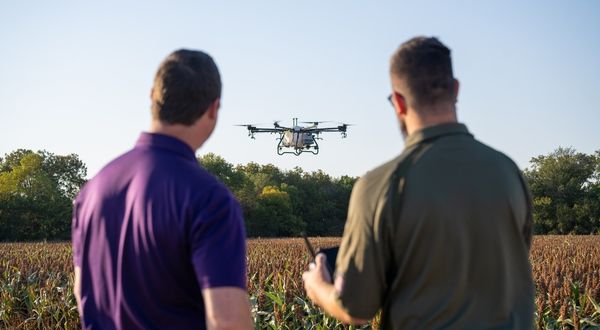 A K-State Salina UAS instructor helps a learner operate a drone over an agriculture field.