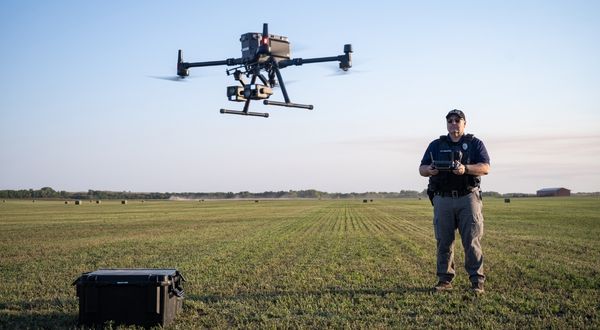 A law enforcement officer flies a drone over an open field.